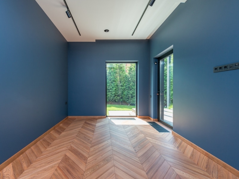 A room with decorative painted walls in a deep blue, timber floors, and a glass door leading to a garden.